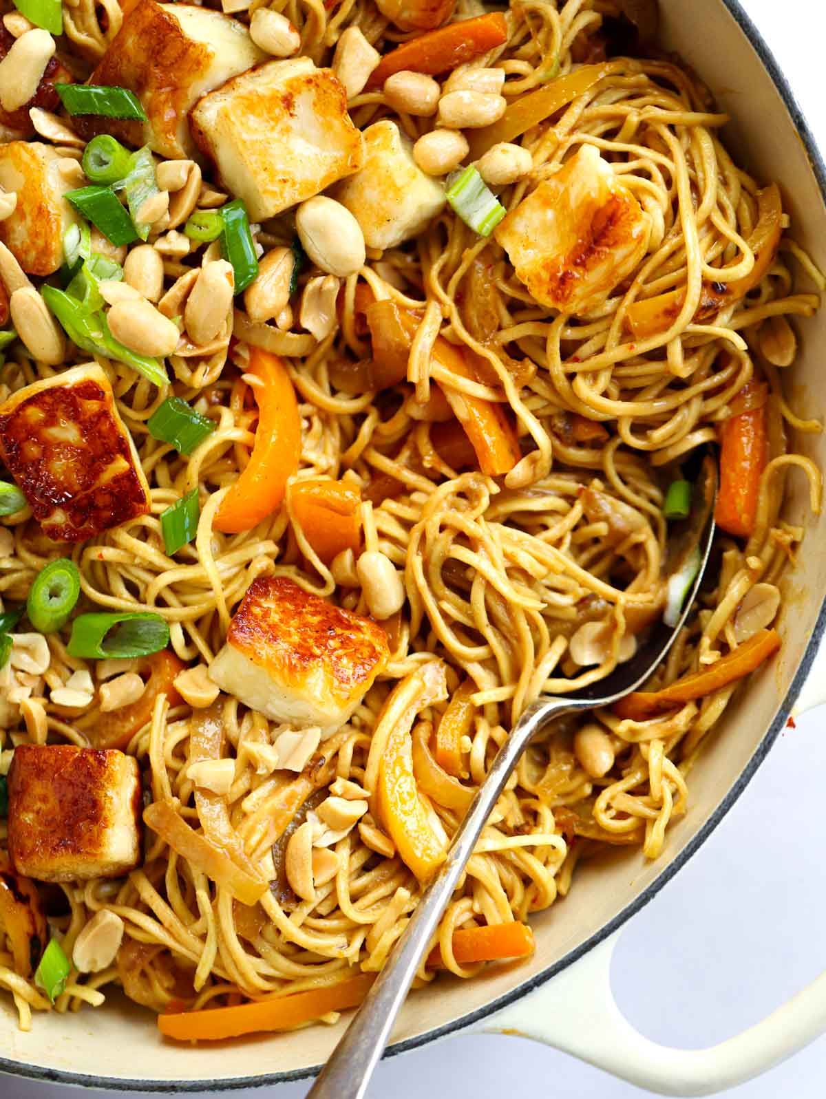A fork in a big pan of noodles with halloumi and satay sauce for Peanut Butter Noodles.