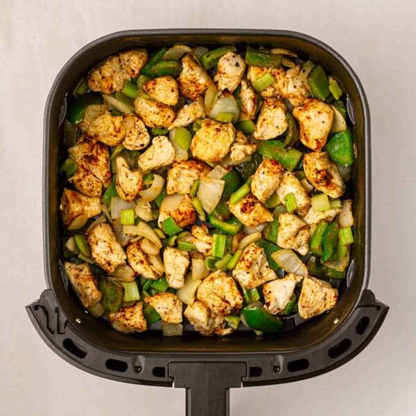 A bird's eye view of an air fryer filled with cajun chicken, green peppers, onion and celery.