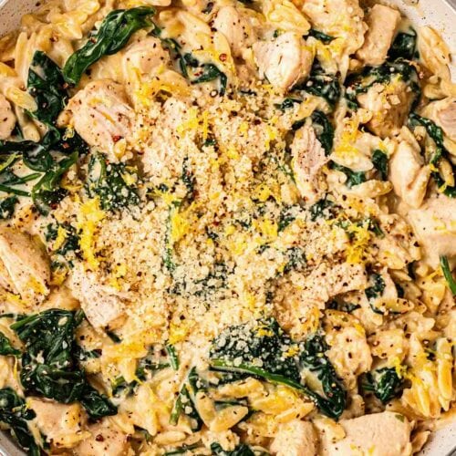 A pan filled with orzo, chicken, spinach, parmesan and lemon, on a table ready to serve.