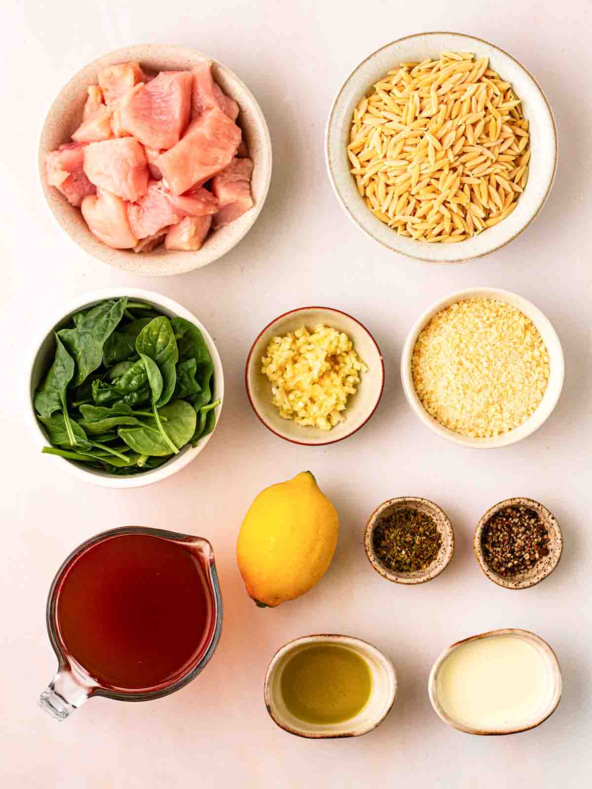 The ingredients for Lemon Chicken Orzo one pot recipe in small bowls on a white counter top.