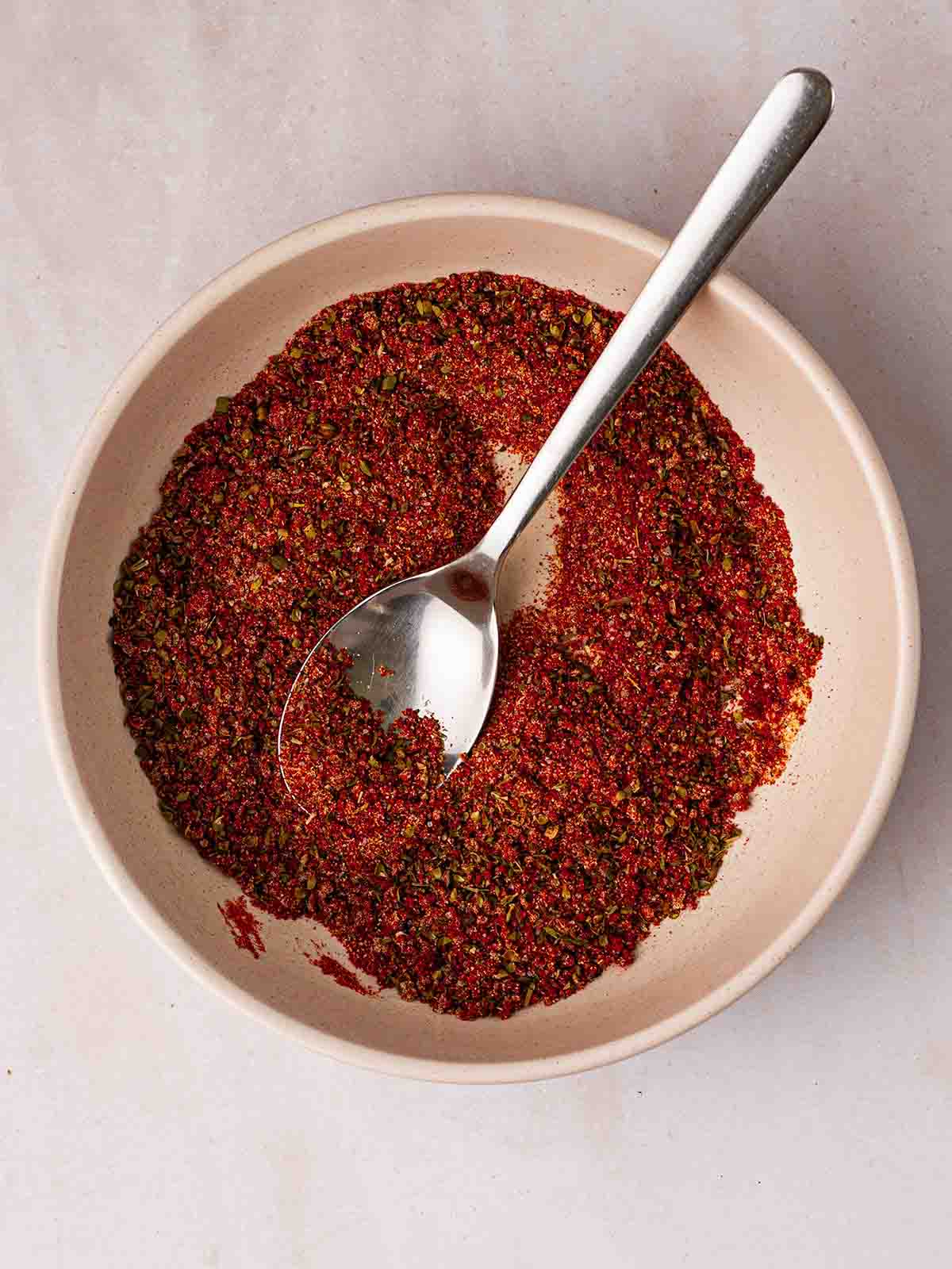 A reddish brown spice mix in a white bowl with a spoon inside.
