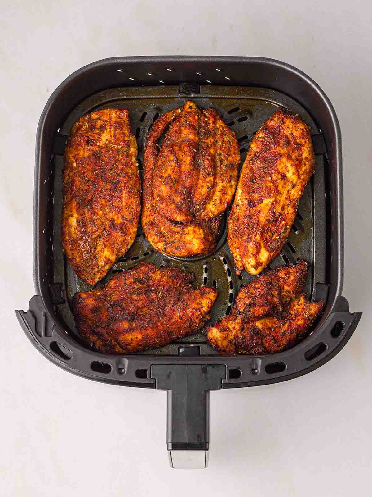 Five chicken cutlets in an air fryer, cooked.