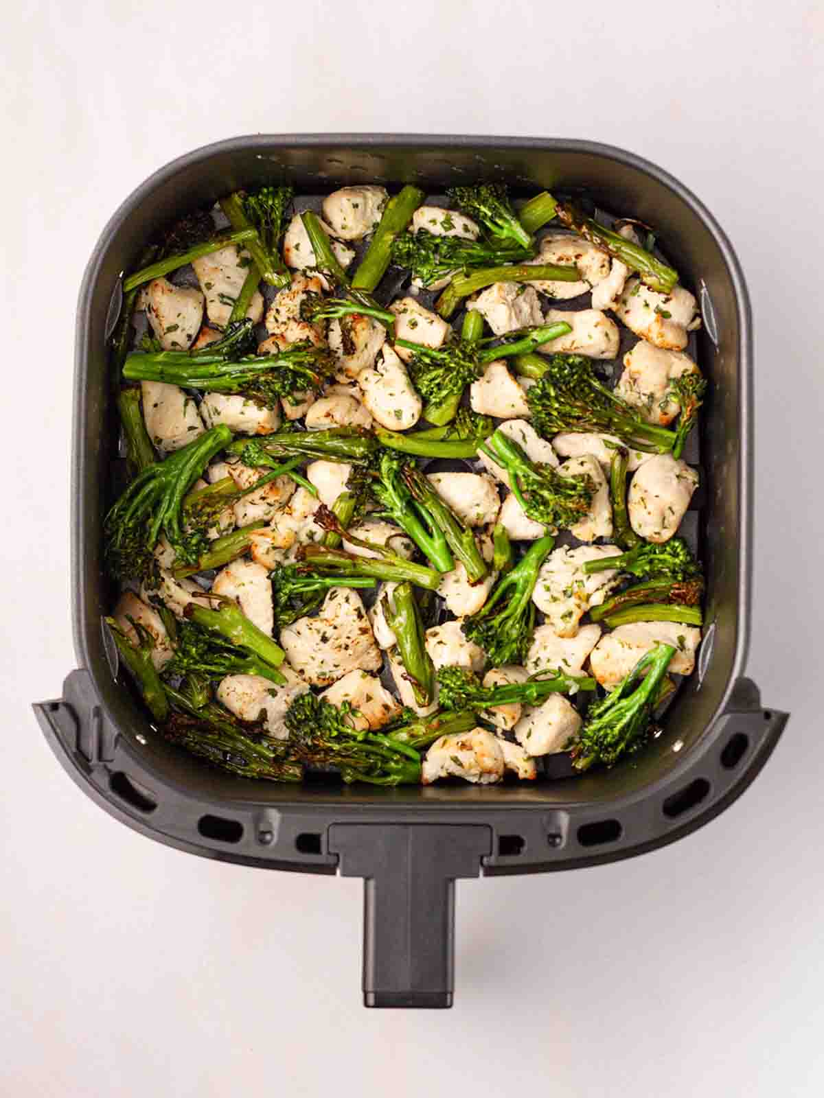 A bird's eye view of an air fryer tray with cooked chicken and broccoli inside for the recipe Garlic Butter Chicken.