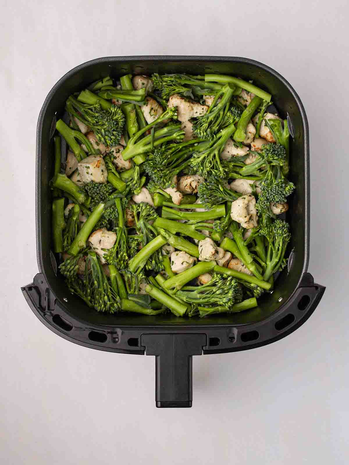 An air fryer filled with cooked chicken and raw broccoli to show step 2 in the recipe for Air Fryer Garlic Butter Chicken.