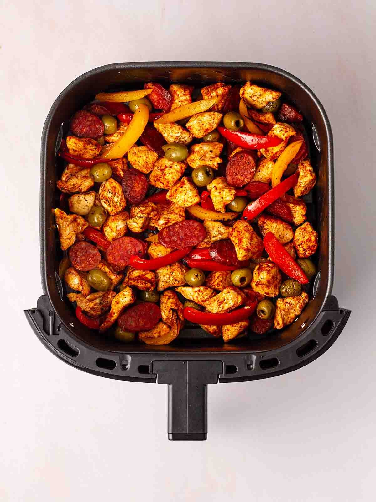 An air fryer filled with chicken, chorizo, olive and peppers for a Spanish style traybake recipe.