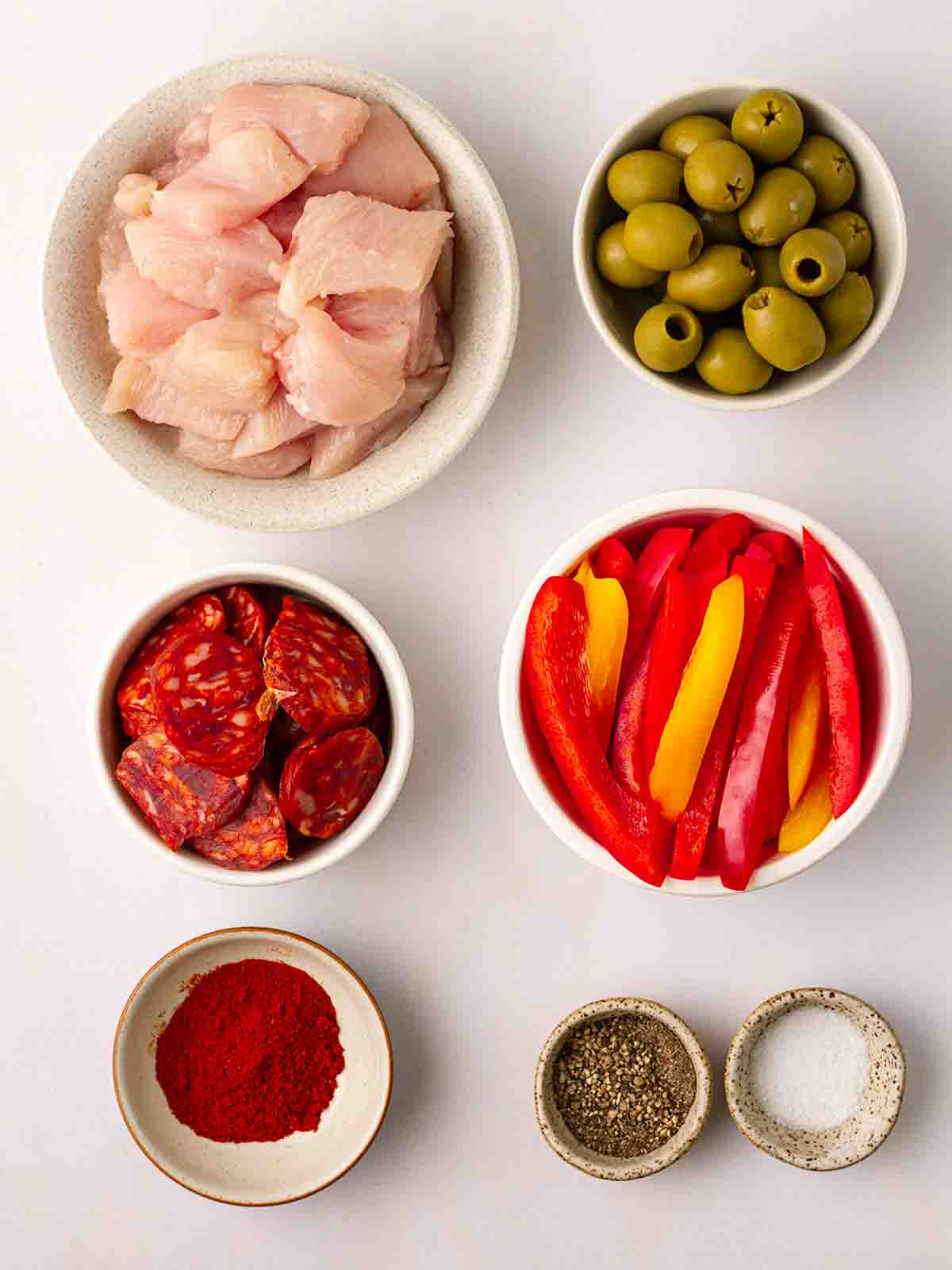 The ingredients for air fryer Spanish chicken chopped and put into bowls on a white counter.
