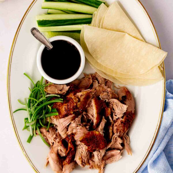 A platter with Peking style crispy duck, cooked in the slow cooker, with pancakes, sauce and cucumber and spring onion on the side.