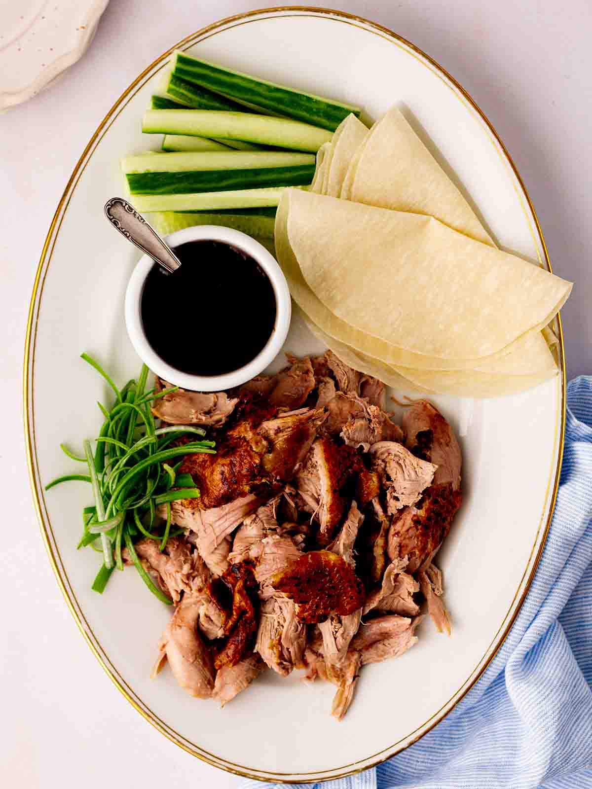 A platter with cooked slow cooker duck shredded, Chinese pancakes, cucumber, spring onion and sauce.